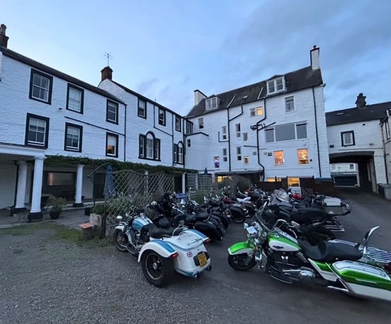 Motorbikes lined up in the hotel car park, with the back of the hotel behind