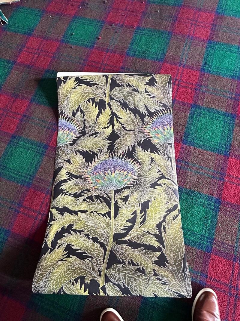A roll of the new thistle wallpaper lying on the old tartan carpet