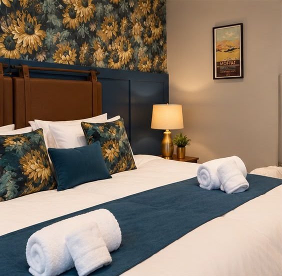 A double bed with a leather headboard, botanical wallpaper and a Moffat poster