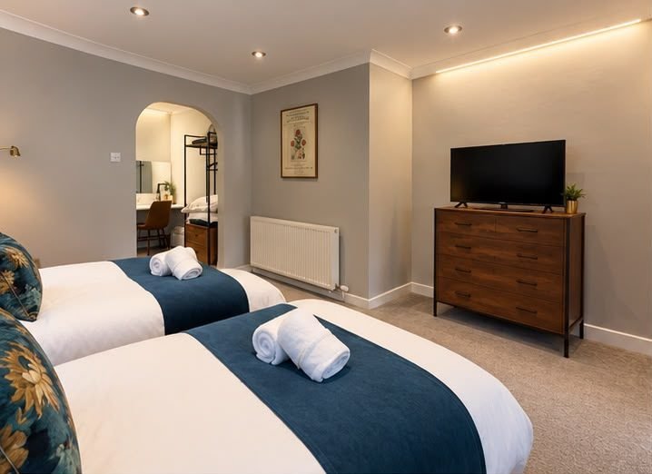 Twin beds made up with blue throws and rolled towels, an archway to the dressing area