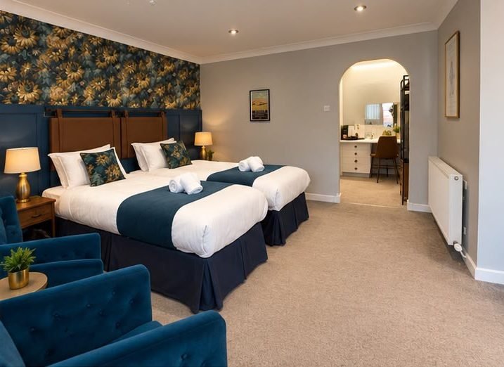 A twin bedroom with blue velvet chairs and an archway through to the dressing area