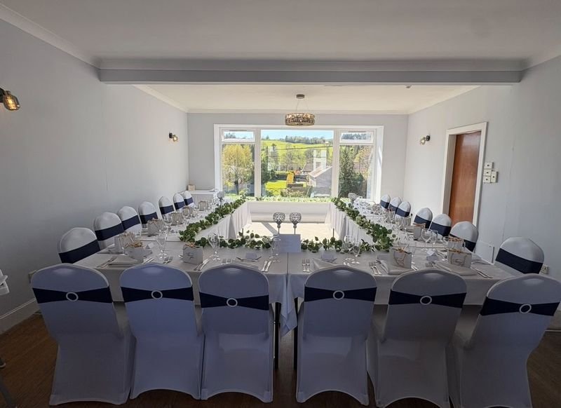 Long tables dressed with greenery, white chair covers with navy sashes