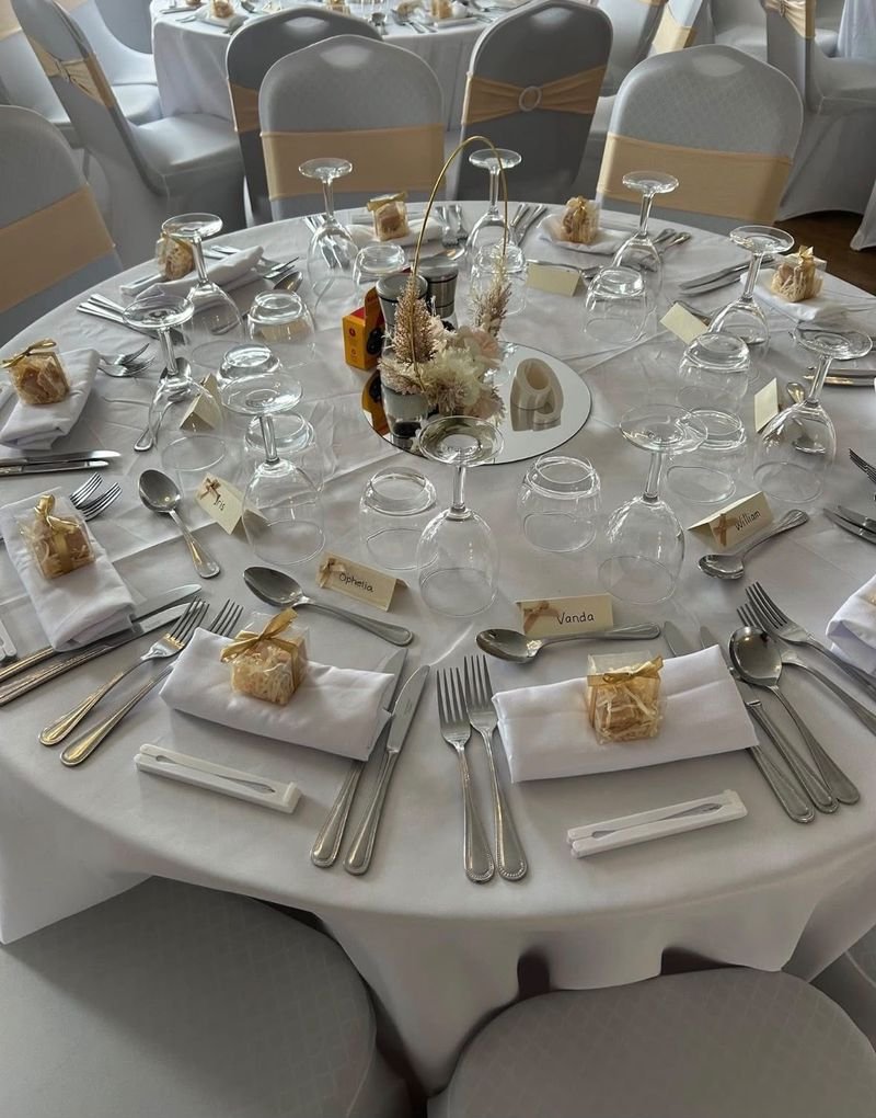 A round table laid for a wedding breakfast, gold sashes on white chair covers