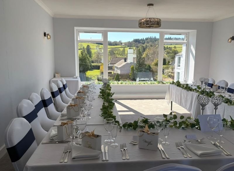 The function room laid for a wedding, the top table in front of a big window onto the hills